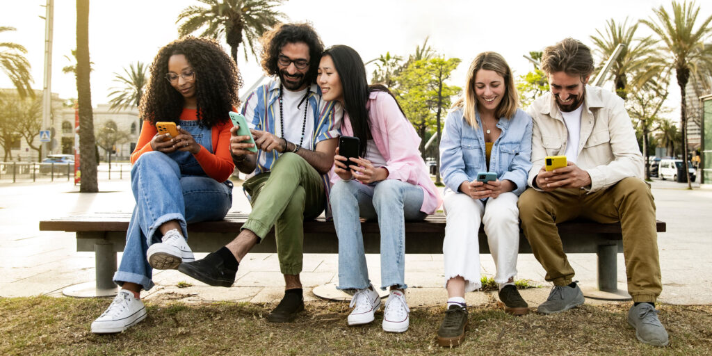 Group of friends sitting outdoors all checking messages on their phones