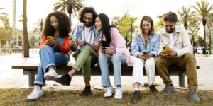 Group of friends sitting outdoors all checking messages on their phones