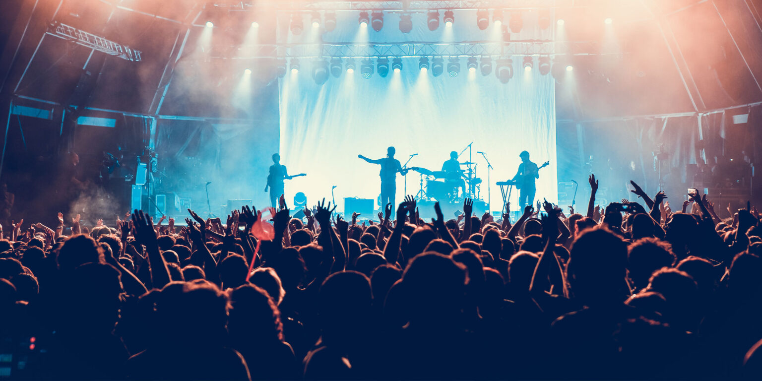 Crowd with raised hands watching a live band perform on stage at a concert